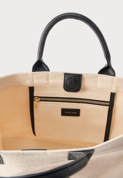 Εσωτερικό μπεζ καμβά τσάντας tote με μαύρες δερμάτινες λαβές, θήκη με φερμουάρ με χρυσό φερμουάρ και μαύρο κλιπ κλεισίματος.