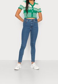 Grön- och vitrandig kortärmad tröja med korta ärmar, kombinerad med blå skinny jeans och vita sneakers. Släta texturer, figursydd design.