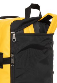 Svart och gul ryggsäck med ficka med dragkedja på toppen, texturerad väv, förstärkt handtag och kontrasterande färgschema.