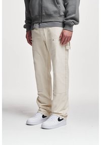Beige cargobroeken van katoen, met meerdere zakken, knoopaccenten en een relaxte pasvorm. Gecombineerd met witte sneakers.
