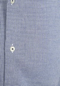 Nahaufnahme von blau-weißer Hahnentrittmuster-Stoff mit zwei weißen Knöpfen, die in einer vertikalen Linie angenäht sind.