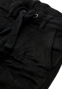 Schwarze Baumwollhosen mit einem Kordelzugbund, ausgestattet mit zwei Vordertaschen und einer subtilen Textur. Die Nähte sind entlang der Seiten sichtbar.