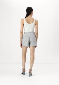 Gray tailored shorts with a textured fabric, two back pockets, and a matching belt. Paired with a white tank top and teal high-heeled sandals.