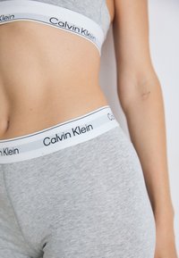 Gray cotton bralette and matching high-waisted briefs with white elastic bands featuring black "Calvin Klein" text along the edges.