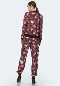 Kwiatowy dres w kolorze bordo z czarnymi akcentami; składa się z kurtki bomberki i zwężanych spodni, obie części mają różnorodne wzory kwiatowe.
