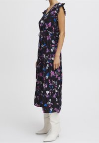 Abito maxi floreale nero con maniche corte a volant, decorato con fiori rosa, bianchi e blu, vita cintrata, abbinato a stivali bianchi con punta.