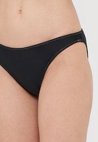 Crni bikini donji dio s minimalističkim dizajnom. Ima kontrastne žute šavove duž rubova, nisku kroj i glatku teksturu.