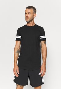 T-shirt nera in cotone a maniche corte con strisce bianche sui polsini. Design a collo rotondo, vestibilità slim e texture liscia.