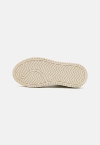 Suola di scarpa in gomma di un beige chiaro con un motivo a zigzag testurizzato e bordi arrotondati, caratterizzata da un marchio di branding all'interno della curva.