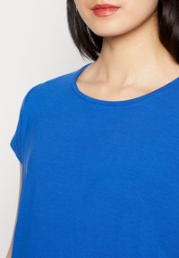 Modrý tričko s krátkým rukávem má hladkou texturu a kulatý výstřih, zobrazující detailní pohled na horní látku.