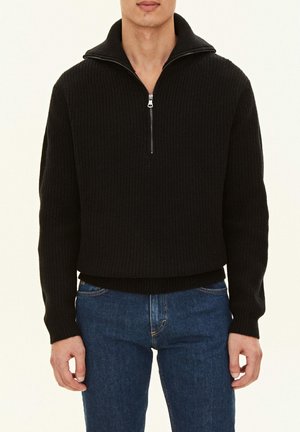 Zwart gebreid sweater met een hoge kraag en halve ritssluiting, met een textuur ribbelontwerp en een cropped pasvorm. Draagt het met blauwe jeans.