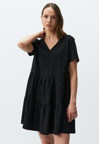 Zwarte, gelaagde jurk in een linnenmix met een V-hals, korte mouwen en textuurstof. Heeft drie geplooide ruffles aan de zoom.