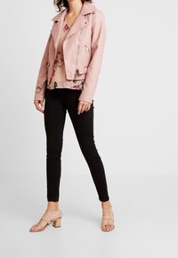 Vaaleanpunainen nahkainen moottoripyörätakki, jossa vetoketjut, käytettynä kukkakuosisen topin päällä, yhdistetty mustiin kapeisiin housuihin ja beigeihin korkolestisenttikenkiin.