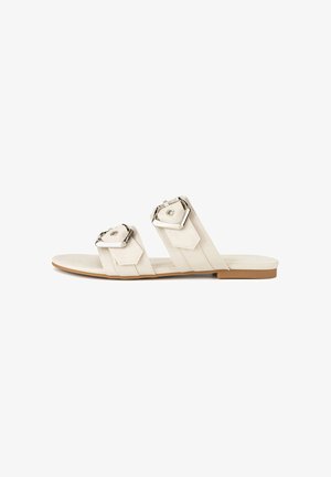White flat sandals with two wide straps featuring square metallic buckles. Smooth texture, minimal design, and a flat rubber sole.