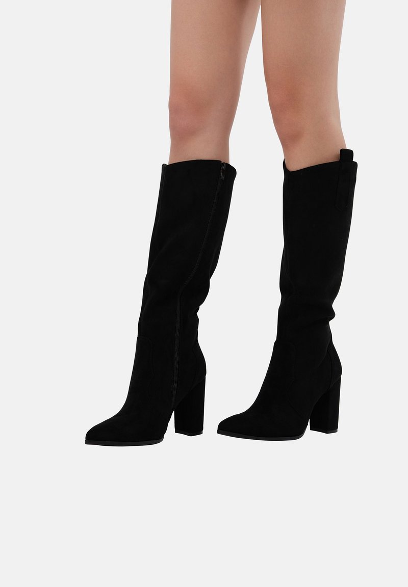 Botas de ante negras hasta la rodilla con punta afilada, tacón cuadrado y cremallera lateral. Presentan un puño plegado en la parte superior y una textura suave.