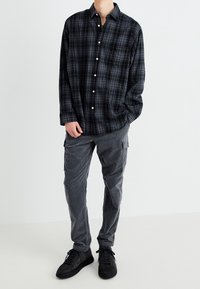 Zwart en grijs geruit overhemd met lange mouwen, gecombineerd met grijze cargobroek en zwarte sneakers, in een ontspannen pasvorm.