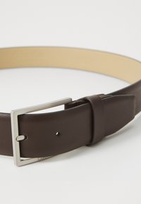 Cinturón de cuero marrón con hebilla de metal plateado. Presenta una textura suave y un interior de color beige claro. Incluye un solo agujero de ajuste.