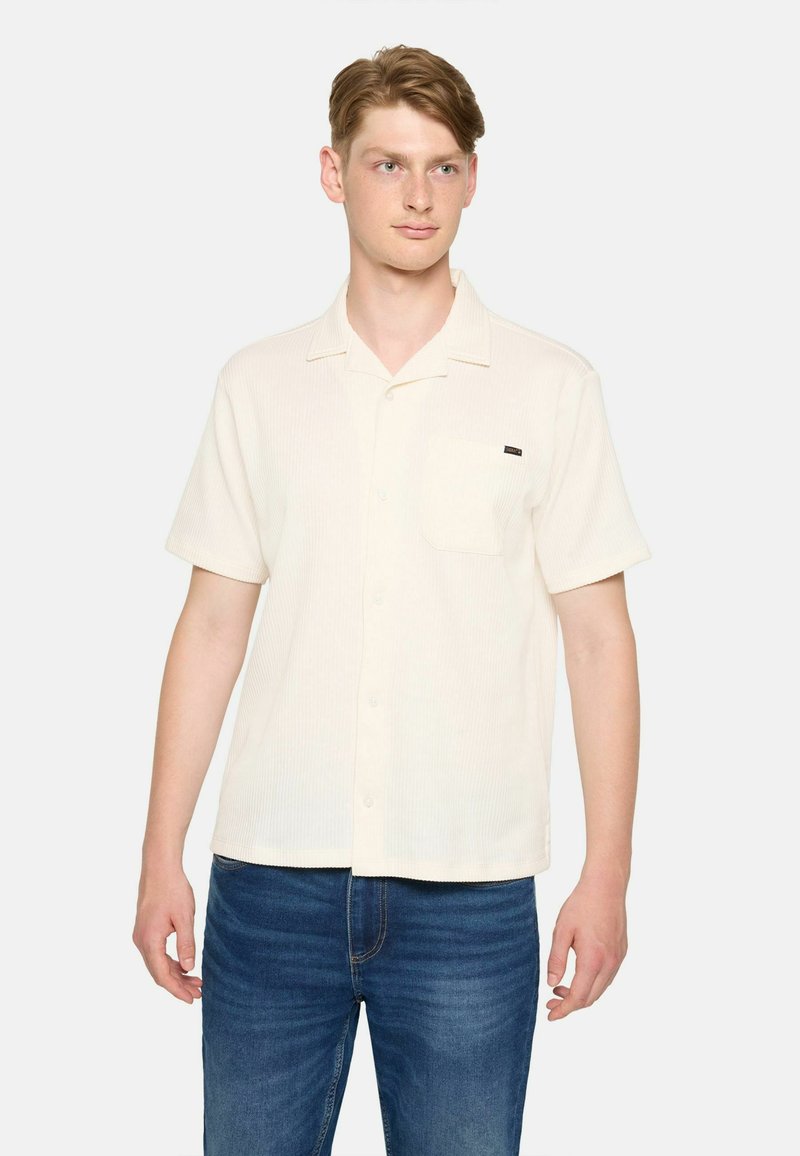 Korte mouw crèmekleurige button-up shirt met een gestructureerde stof, een enkele borstzak en een subtiele labelaccent op de zak. Gecombineerd met blauwe jeans.