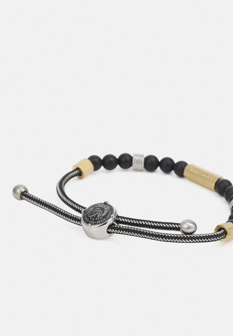 Schwarzes geflochtenes Armband mit Silber- und Goldakzenten, ausgestattet mit runden schwarzen Perlen und einem runden metallischen Charm mit eingraviertem Design.