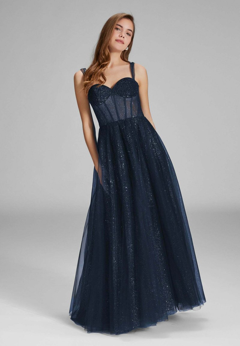 Robe de soirée bleu marine avec un corsage ajusté, un haut transparent et une jupe en tulle évasée. Présente une texture étincelante et des bretelles réglables.