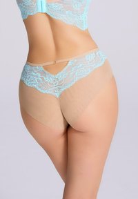 Koronkowe majtki w jasnoniebieskim kolorze z przejrzystym cielistym tyłem, zdobione kwiatowymi wzorami i dekoracyjnym złotym pierścionkiem. Gładka tekstura.