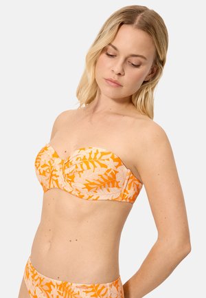 Mujer vistiendo un bikini sin tirantes con estampado floral en tonos naranja y beige, con parte superior y parte inferior a juego, mirando hacia abajo con expresión relajada sobre un fondo liso.
