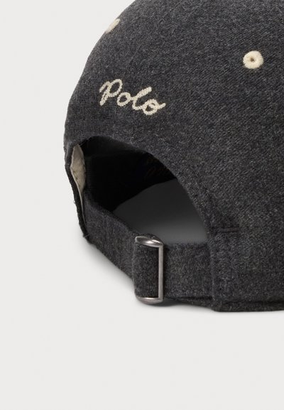 Tumehall villane müts, millel on kerge kergelt kreemikas "Polo" tikand, hõbedane reguleeritav metallrihm taga ning tekstuuriga kangas.