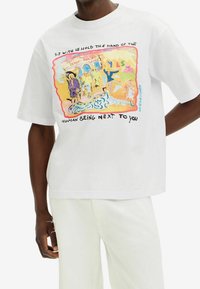 Biała bawełniana koszulka z kolorową grafiką i tekstem. Luźny krój, krótki rękaw i okrągły dekolt.