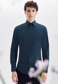 Granatowa koszula z długim rękawem i klasycznym kołnierzykiem, z delikatnym wzorem w kropki. Materiał ma gładką teksturę.