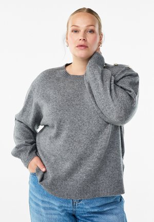 Grey knitted sweater with a wide neckline, dropped shoulders, and ribbed cuffs. Features gold buttons on the shoulder. Worn with blue jeans.
