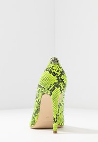 Escarpin avec un motif de peau de serpent noir et vert fluo, bout pointu et talon fin. Accent métallique au dos.