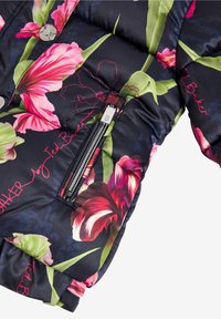 Chaqueta acolchada floral con fondo negro, presenta flores en tonos rosa brillante y verde, un bolsillo con cremallera y botones a presión plateados.