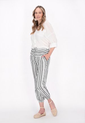 Camicia bianca con bottoni abbinata a pantaloni joggers a righe bianche e nere. L'outfit presenta una vestibilità rilassata e una cintura elastica, completato da espadrillas beige.