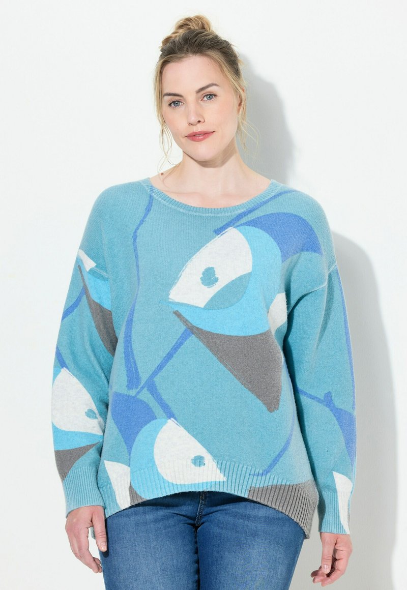 Ljusblå tröja med abstrakta fiskmönster i mörkare blått och grått. Ribbad nederkant och ärmslut, avslappnad passform, texturerat stickat material.