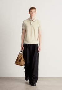 Μπεζ πόλο πουκάμισο με κοντά μανίκια και ριγωτό γιακά, σε συνδυασμό με φαρδιά μαύρη παντελόνια και καφέ τσάντα. Λείο ύφασμα και καθημερινός σχεδιασμός.