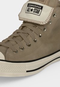 Μπεζ ψηλοτά αθλητικά παπούτσια Converse All Star με μεταλλικές τρύπες, μπεζ κορδόνια, λευκή λαστιχένια σόλα και λεπτομέρεια με μαύρη ρίγα.