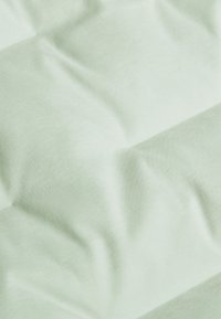 Jasnozielony materiał o miękkiej, gładkiej fakturze z pikowanym wzorem nakładających się paneli, tworzącym wrażenie wypukłości.