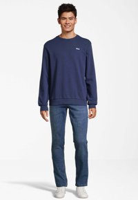 Felpa girocollo blu navy con logo Fila, abbinata a jeans in denim blu e sneakers bianche, con maniche lunghe e polsini a coste.