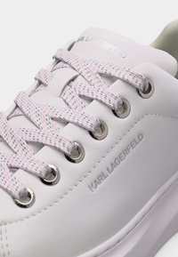 Κοντινό πλάνο λευκού αθλητικού παπουτσιού Karl Lagerfeld με ροζ και γκρι κορδόνια με μοτίβο και επώνυμα ασημένια κουμπώματα.
