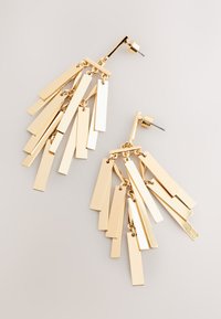 Guldfärgade örhängen med hängande rektangulära metallbitar i olika längder, som skapar en fransliknande effekt. Polerad yta och stiftöppning med låsning bak.