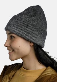 Grau gestrickte Beanie mit gerippter Textur, leicht spitz zulaufender Krone, die auf einer Person getragen wird, die ein beigefarbenes Shirt und eine braune Jacke trägt.