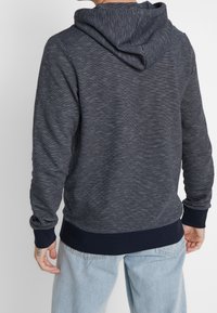Marineblauwe en witte gestreepte hoodie met een capuchon met trekkoord, geribbelde manchetten en zoom. Zachte stof, ontspannen pasvorm en een gestructureerd oppervlak.