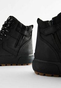 Czarne wysokie buty z cholewką z teksturowanej tkaniny, z zamkami błyskawicznymi, wzmocnionymi oczkami i solidną podeszwą z wielokierunkowym bieżnikiem.