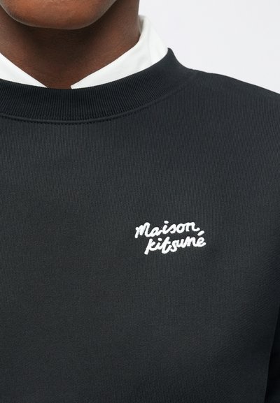 Sudadera negra de punto con cuello acanalado, que presenta un logo bordado en blanco "Maison Kitsuné" en el pecho. Textura suave, diseño minimalista.