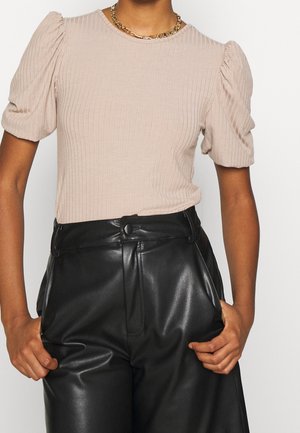 Ribbed beige short-sleeve top with puffed sleeves worn with high-waisted black leather pants and a gold chain necklace.