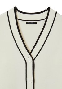 Cardigan bianco con bordature nere lungo il collo a V e la patta dei bottoni, con due bottoni bianchi e una piccola etichetta del brand all'interno del colletto.