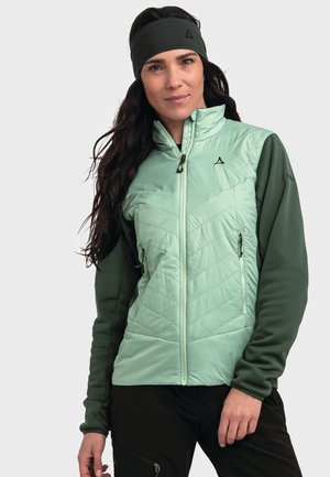 Hellgrüne isolierte Jacke mit gestepptem Muster, grünen Ärmeln, zwei Reißverschlusstaschen und einem hohen Kragen. Getragen mit einem passenden Stirnband.