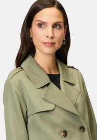 Helle olivgrüne Trenchcoat mit doppelter Knopfleiste, großen Revers und zwei Frontknöpfen. Glattes Material mit taillierter Passform.