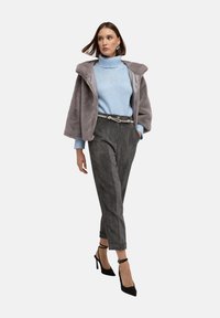 Grijze nepbontjas, lichtblauwe gebreide trui, antracietkleurige corduroy broek, zwarte stilettohakken. Soepele textuur en gelaagd ontwerp.