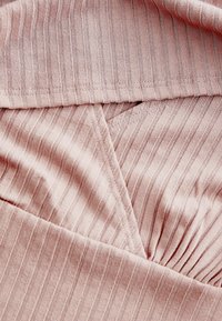 Tissu côtelé rose clair avec de fines lignes verticales, présentant une section plissée et un design superposé au niveau de l'encolure. Texture lisse.